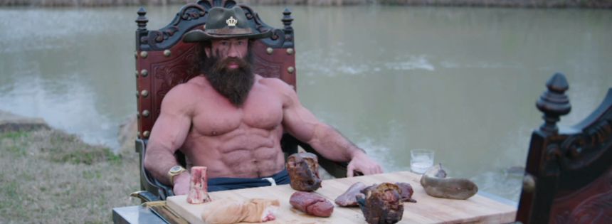 A muscular shirtless bearded man on an ornate throne with cuts of meat, the hyper-masculine carnivore stereotype