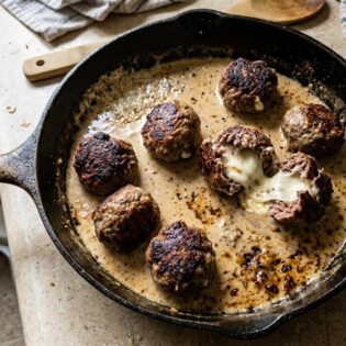 Carnivore meatballs in a cast iron pan, one broken open with melted mozzarella stretching out