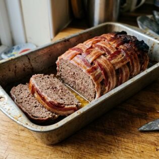 Carnivore meatloaf with a bacon lattice top, two slices cut, resting in a battered loaf tin