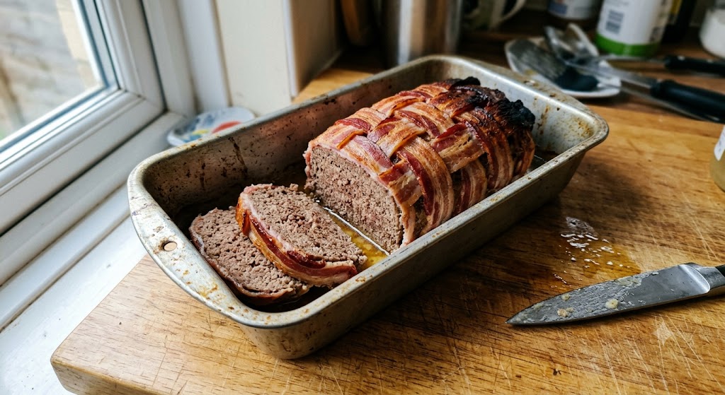 Carnivore meatloaf with a bacon lattice top, two slices cut, resting in a battered loaf tin