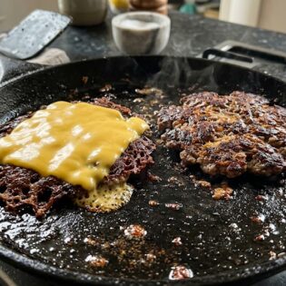 Two carnivore smash burger patties with melting cheese on a cast-iron pan