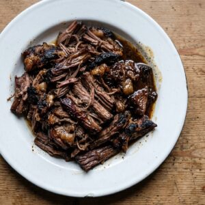 Pulled slow roast mutton shoulder on a white enamel plate with its own pan juices spooned over