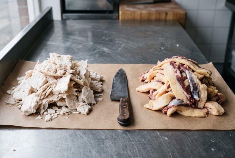 Raw beef suet, white and crumbly with papery membrane, beside softer yellow beef trim streaked with red meat, on butcher’s paper on a steel counter